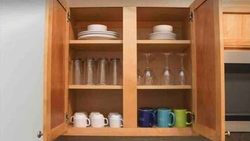 A wooden cabinet with shelves containing plates, glassware, and mugs.