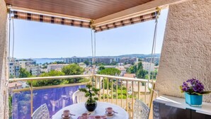 En balkon med et bord dækket til the, med udsigt over en by der inkluderer bygninger og et vandområde.