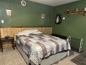 Une chambre à coucher avec une tête de lit en bois, une couvre-lit matelassée, une table de chevet avec une horloge et une étagère ornée d’objets décoratifs.