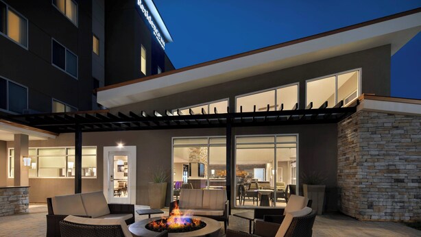 An outdoor patio area with wicker furniture, a fire pit, and a view of the interior dining area. - Residence Inn by Marriott Waco South (Waco)