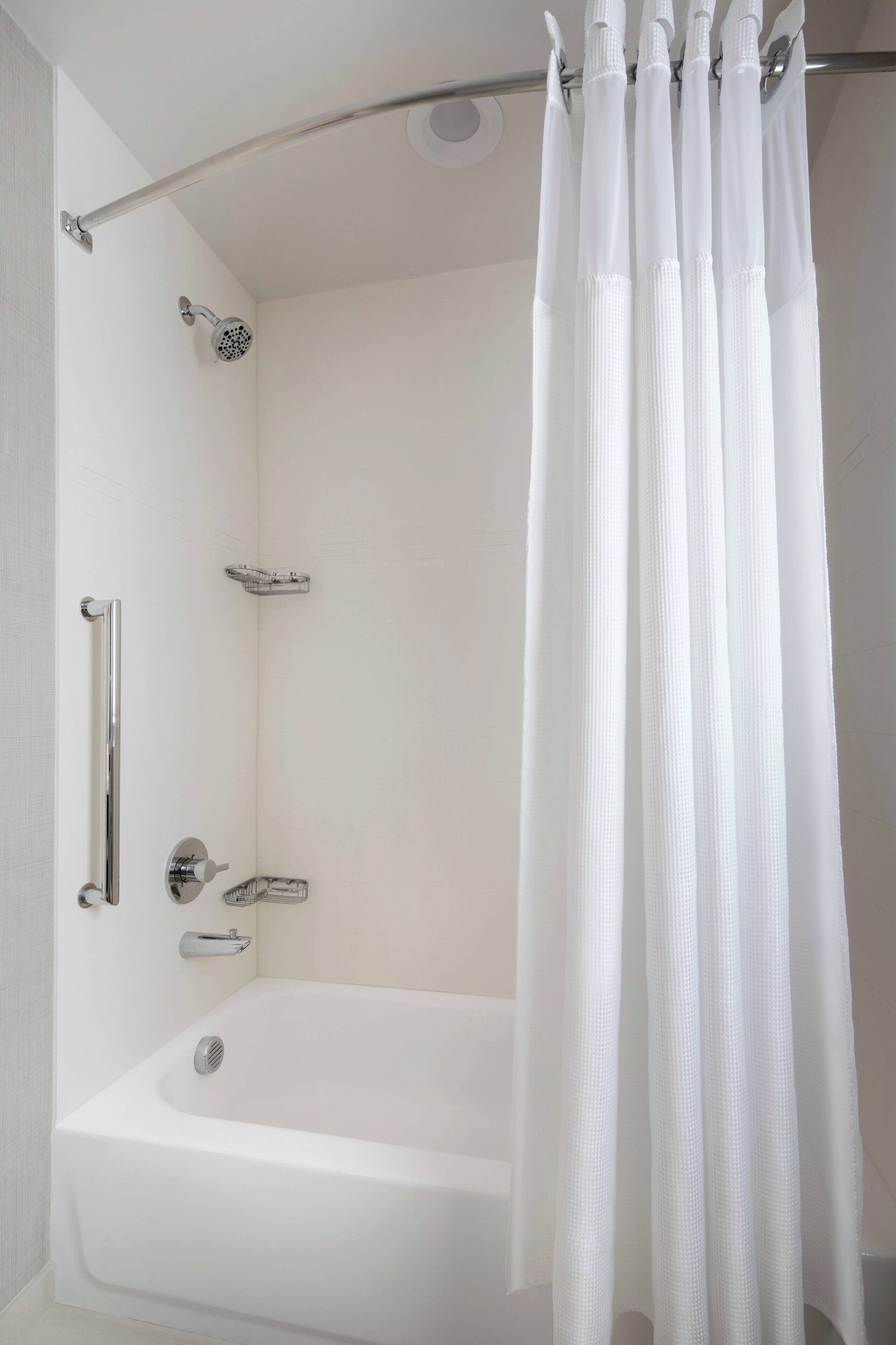 A modern bathroom with a white bathtub, a handheld showerhead, and a glass shower enclosure.
