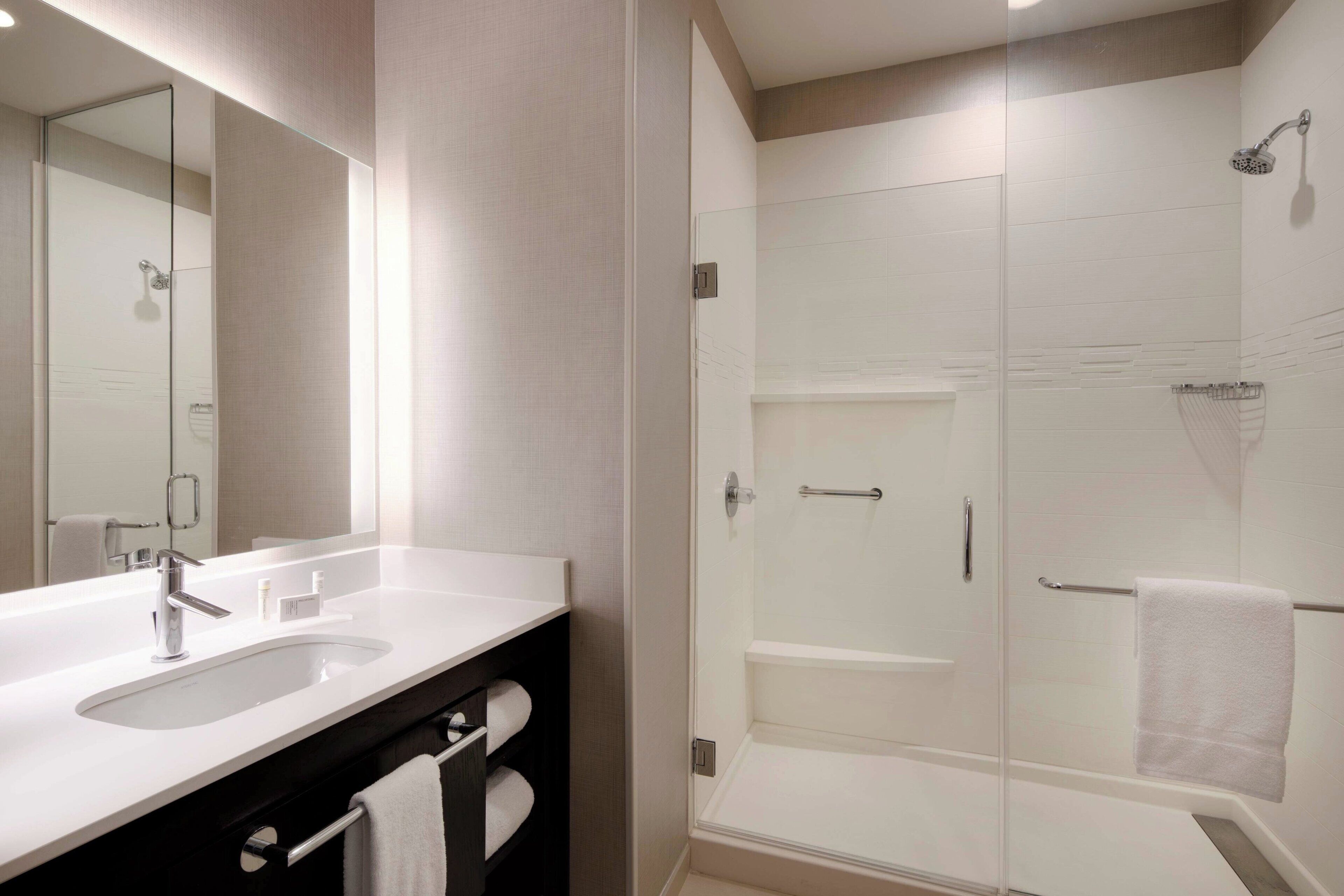 A modern bathroom with a large mirror, a sink, a shower, and a towel rack.