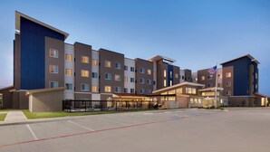 A multi-story hotel with a modern design, featuring a mix of brown and blue exterior panels, a prominent American flag, and a well-lit entrance. - Residence Inn by Marriott Waco South (Waco)