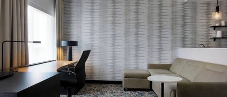 Une chambre d’hôtel moderne équipée d’un bureau, d’un fauteuil de bureau, d’un canapé et d’une petite table ronde.