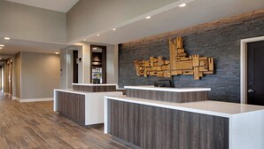 A reception area with a modern design, featuring a stone wall with a wooden cityscape artwork, a reception desk, and a wooden floor. - Residence Inn by Marriott Waco South (Waco)