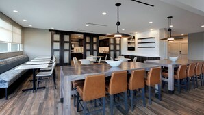 A modern dining area with a large wooden table, multiple seating options, and pendant lighting. - Residence Inn by Marriott Waco South (Waco)