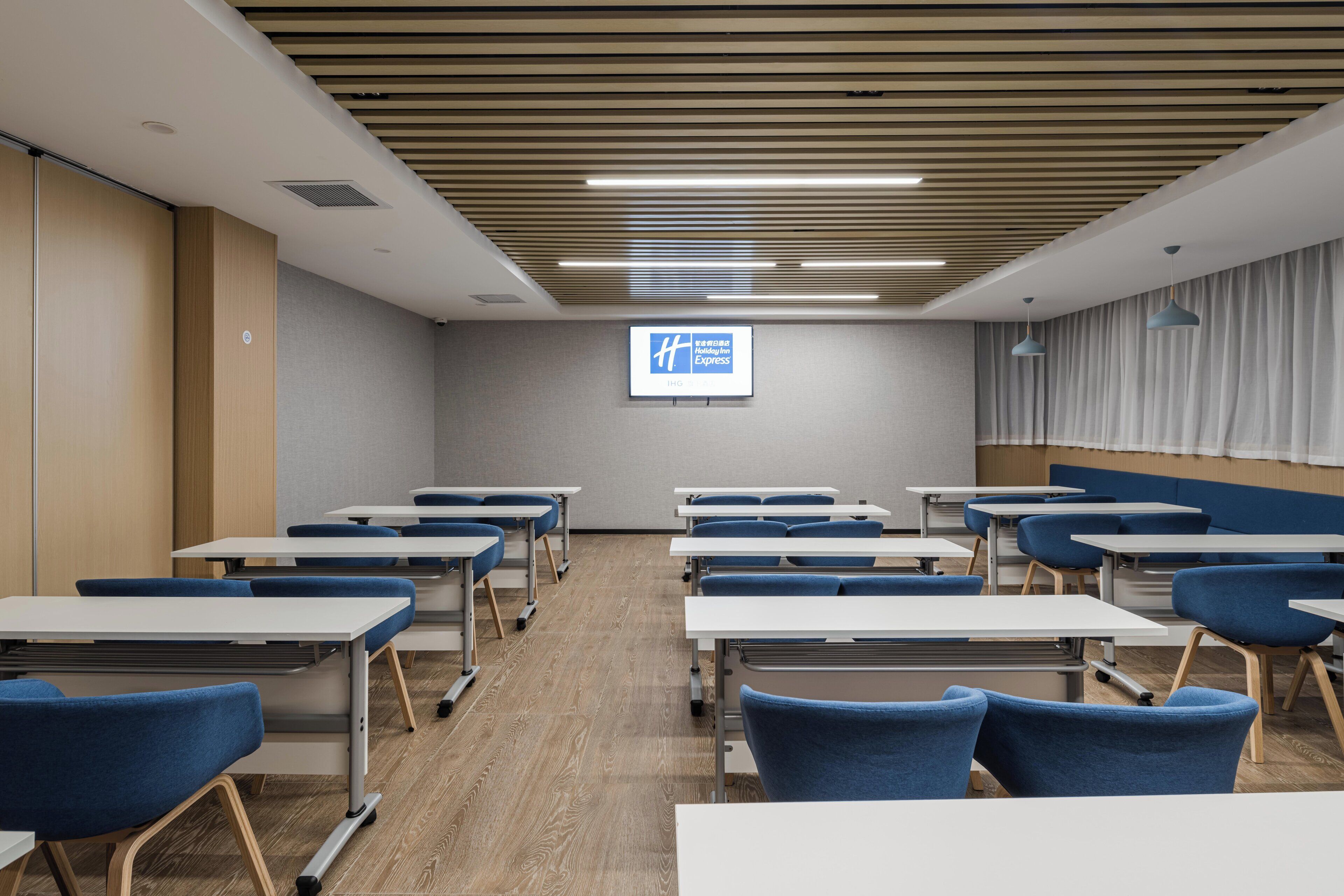 A conference room with tables and chairs, a projector screen, and a sign for Holiday Inn Express.