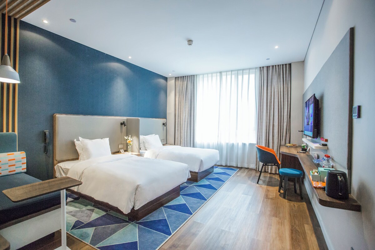 Ein Hotelzimmer mit zwei Betten, einem Schreibtisch, einem Stuhl, einem Fernseher und einem Badezimmer.