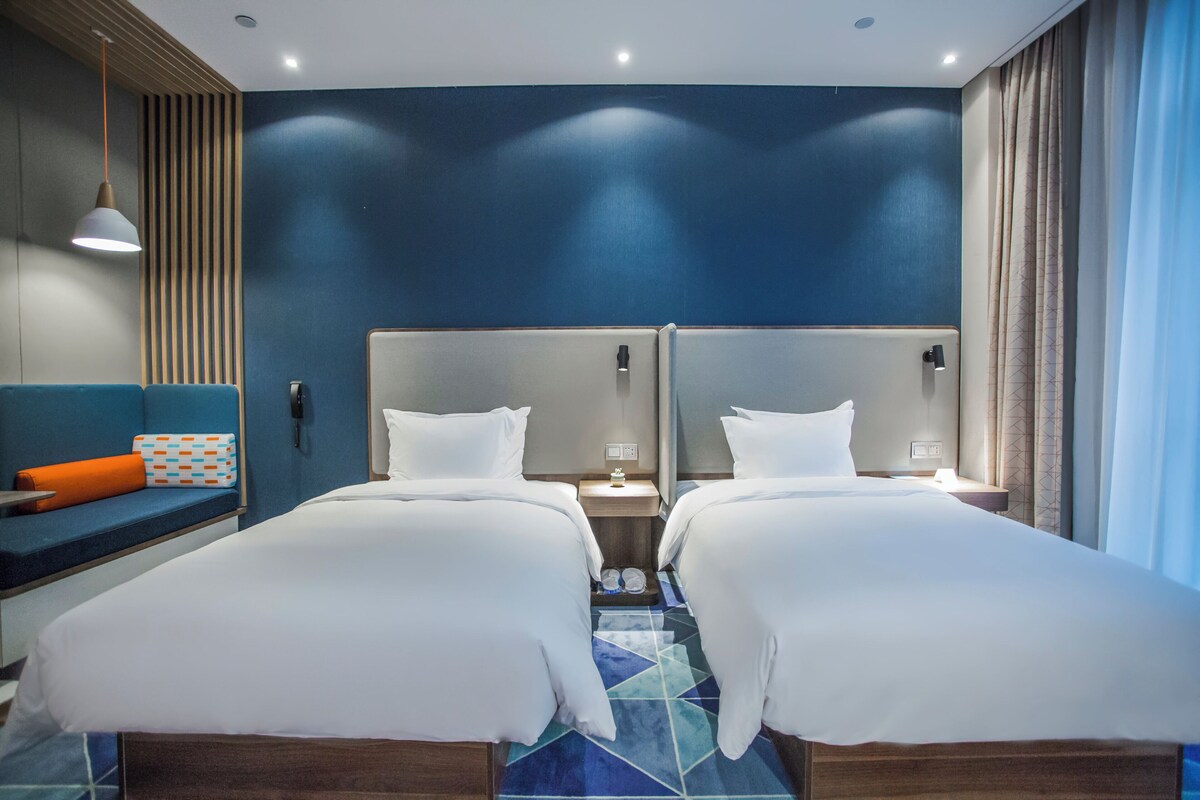 Ein Hotelzimmer mit zwei Betten, einer Sitzecke mit einem gemusterten Kissen und Blick auf den Nachthimmel.