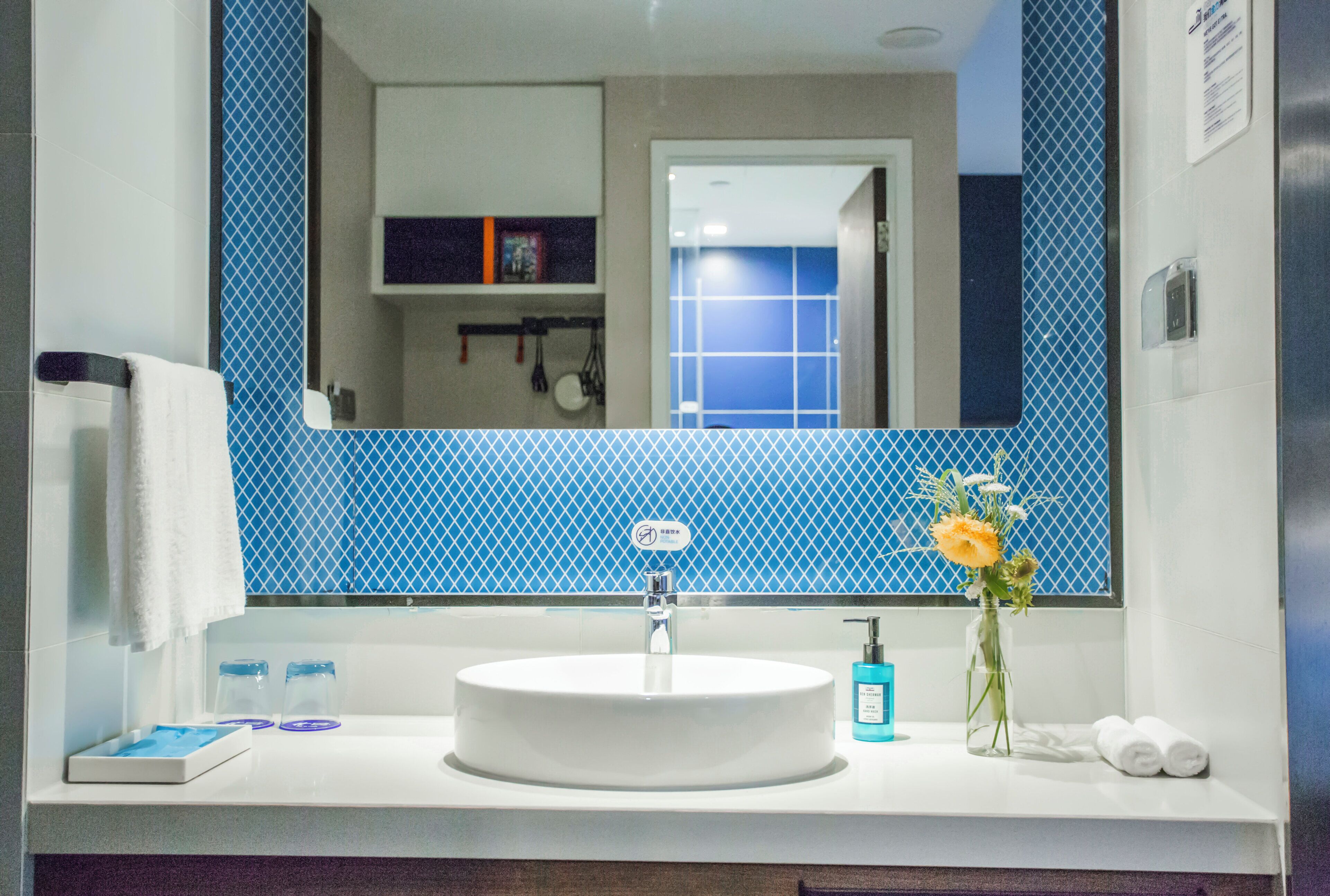 A bathroom with a round sink, a mirror, and a vase with flowers.