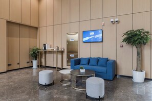 Um lobby moderno com um sofá azul, uma máquina de café, uma tela de televisão e um vaso de planta.