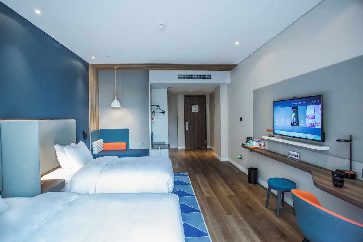 Ein Hotelzimmer mit Bett, Schreibtisch, Stuhl, Fernseher und einem Badezimmer im Hintergrund.