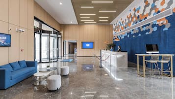 A modern lobby with a reception desk, seating area, and a large digital display.