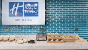 A hotel room with a blue brick wall, a flat-screen TV displaying the Holiday Inn Express logo, a marble countertop with various breakfast items, and electrical outlets. - Holiday Inn Express Pudong Chuansha by IHG (Shanghai)
