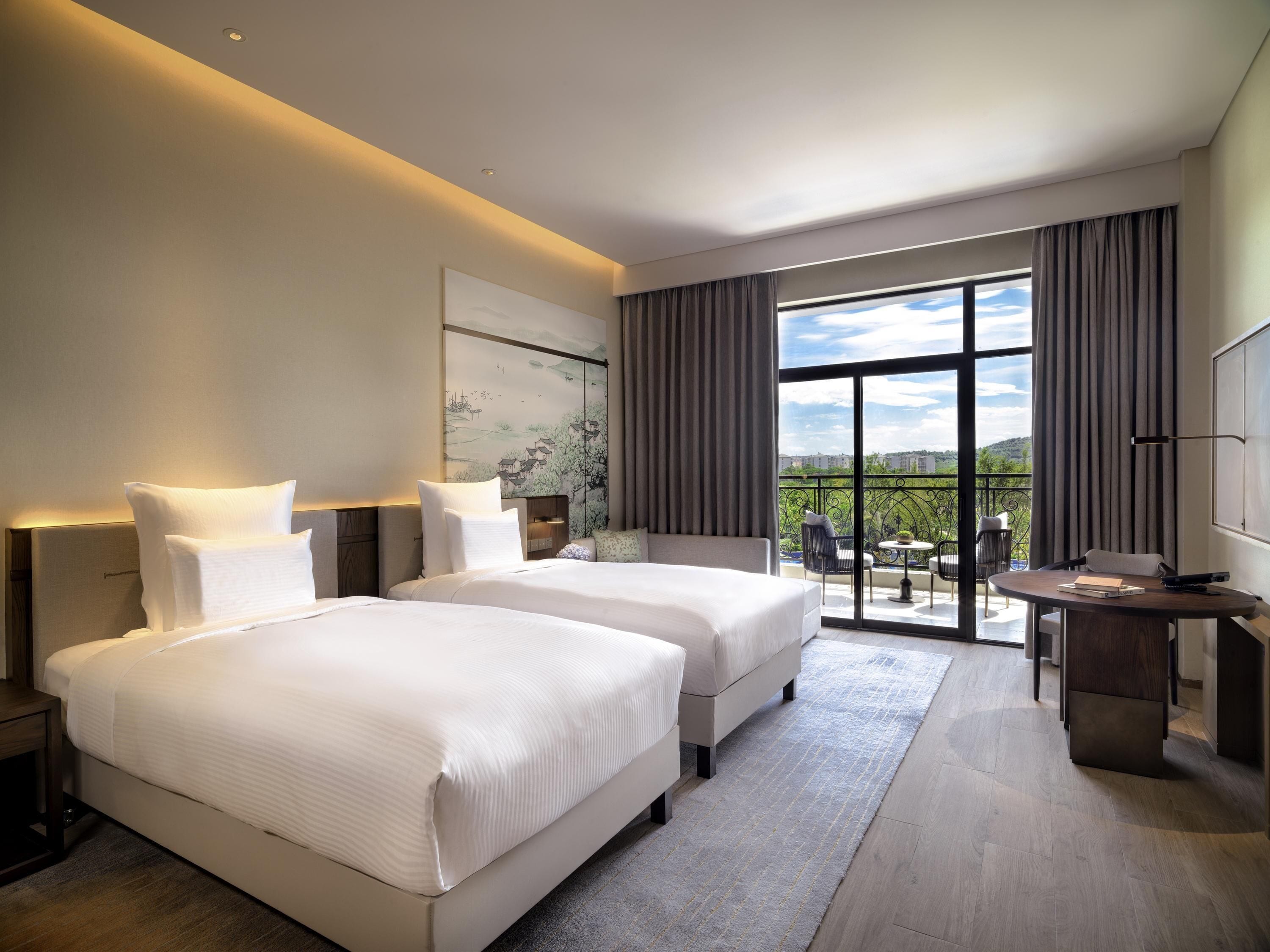 A hotel room with two beds, a balcony with a view, a desk, and a TV.