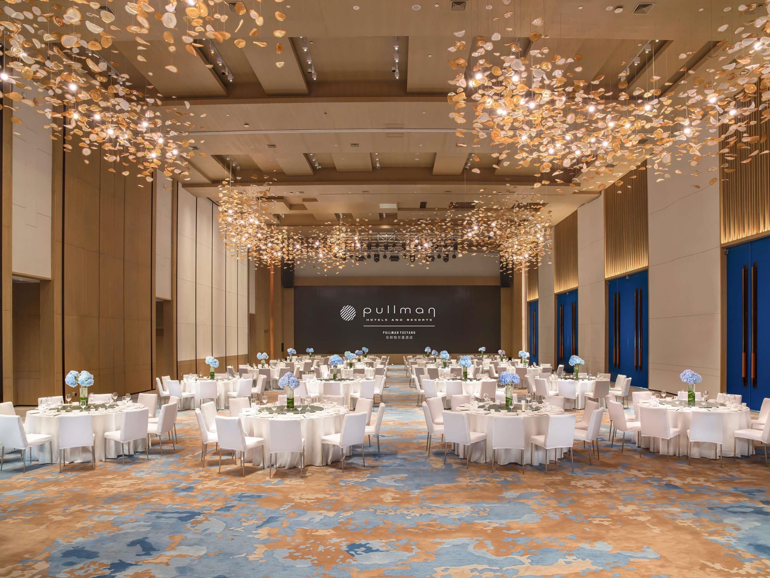 A hotel ballroom with round tables, white chairs, and a large screen displaying the hotel name.