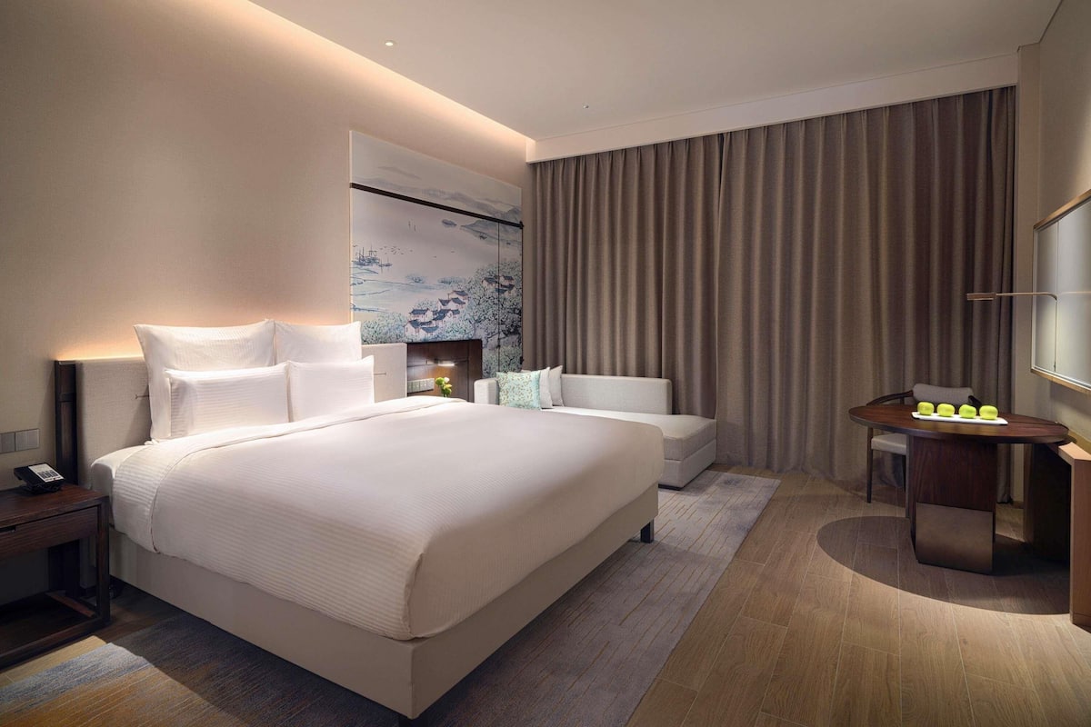 A modern hotel room with a large bed, bedside tables, a desk, and a chair.