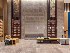 Un vestíbulo moderno con pisos de mármol, un mostrador de recepción y dos grandes estanterías con paneles decorativos.