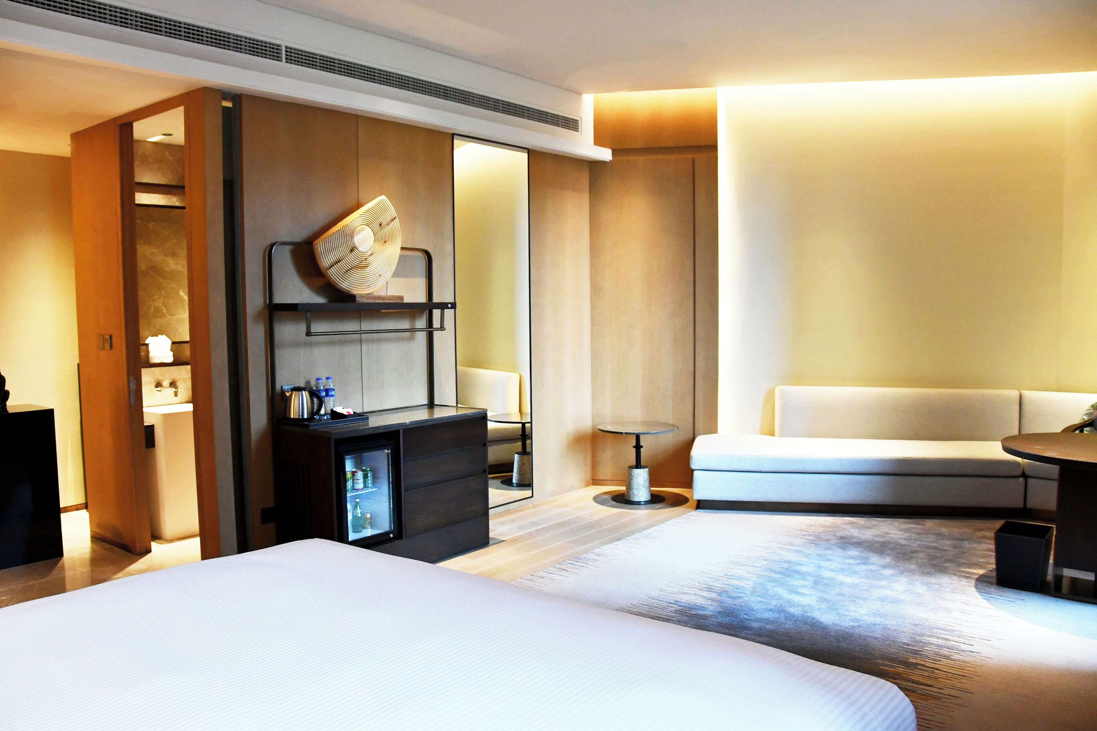 A hotel room with two beds, a sofa, a small table, a minibar, and a mirror.
