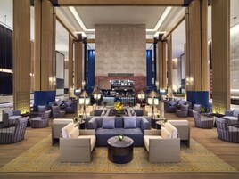 A spacious lobby with a central seating area, a bar, and a high ceiling with a large stone wall.