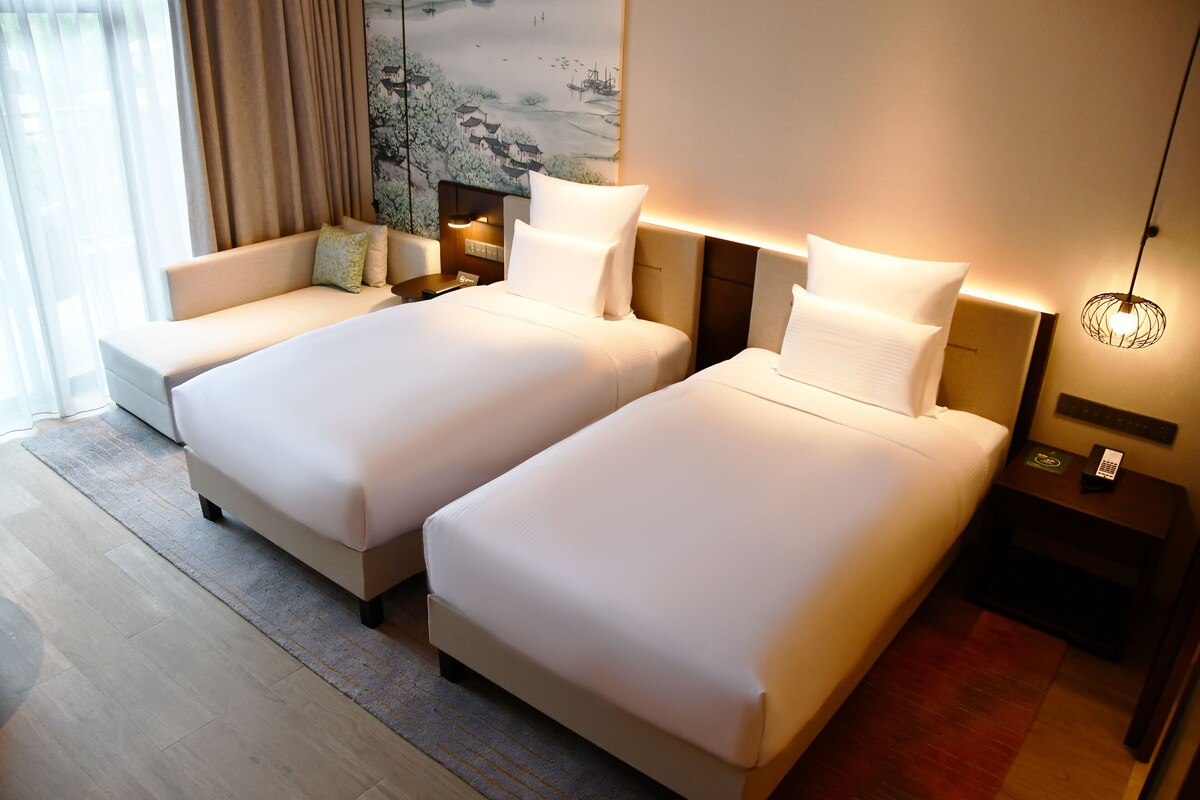 A hotel room with two beds, a sofa, a nightstand with a lamp, and a painting on the wall.