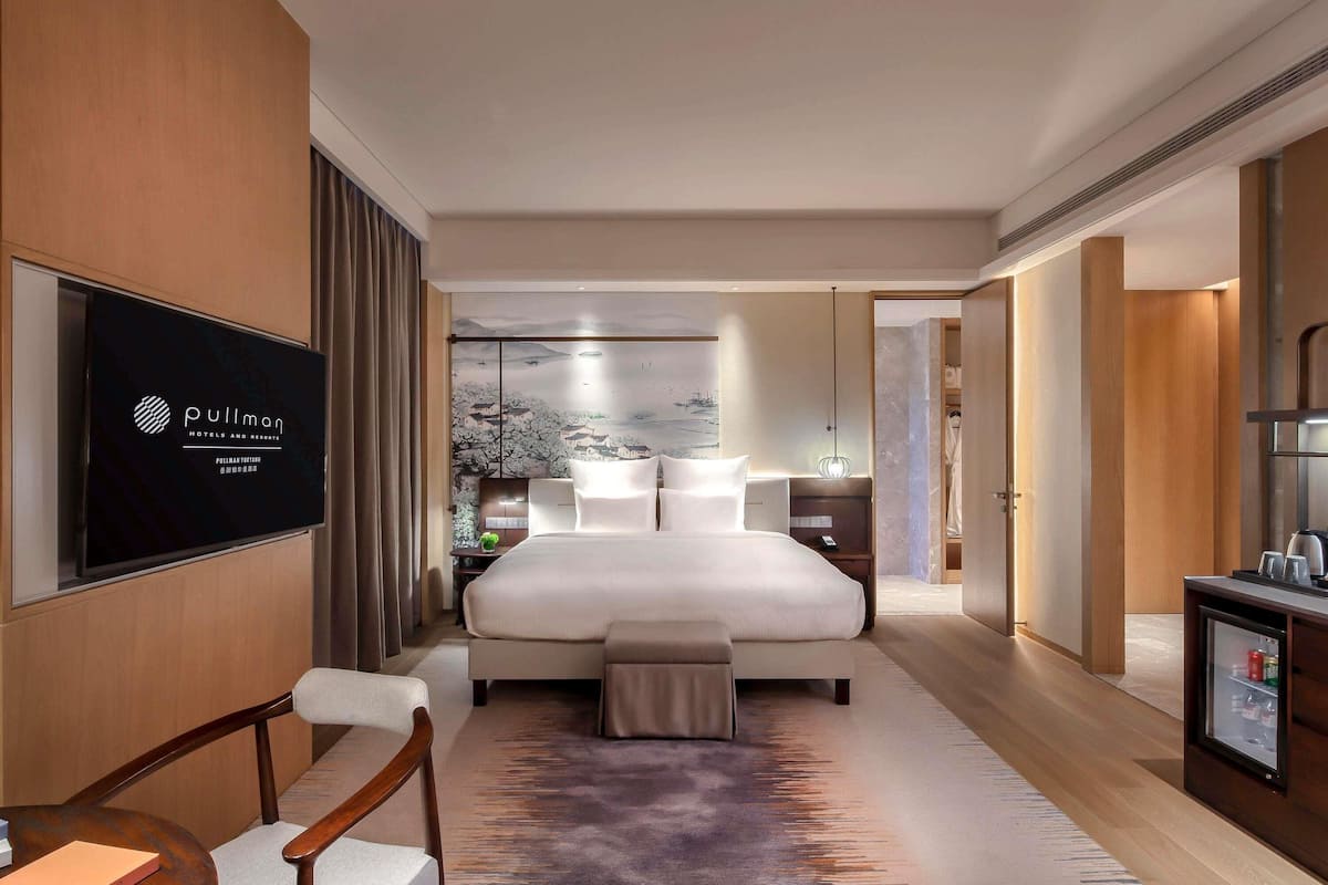 A hotel room with a large bed, a desk with a chair, a TV, and a view of a traditional building through a window.