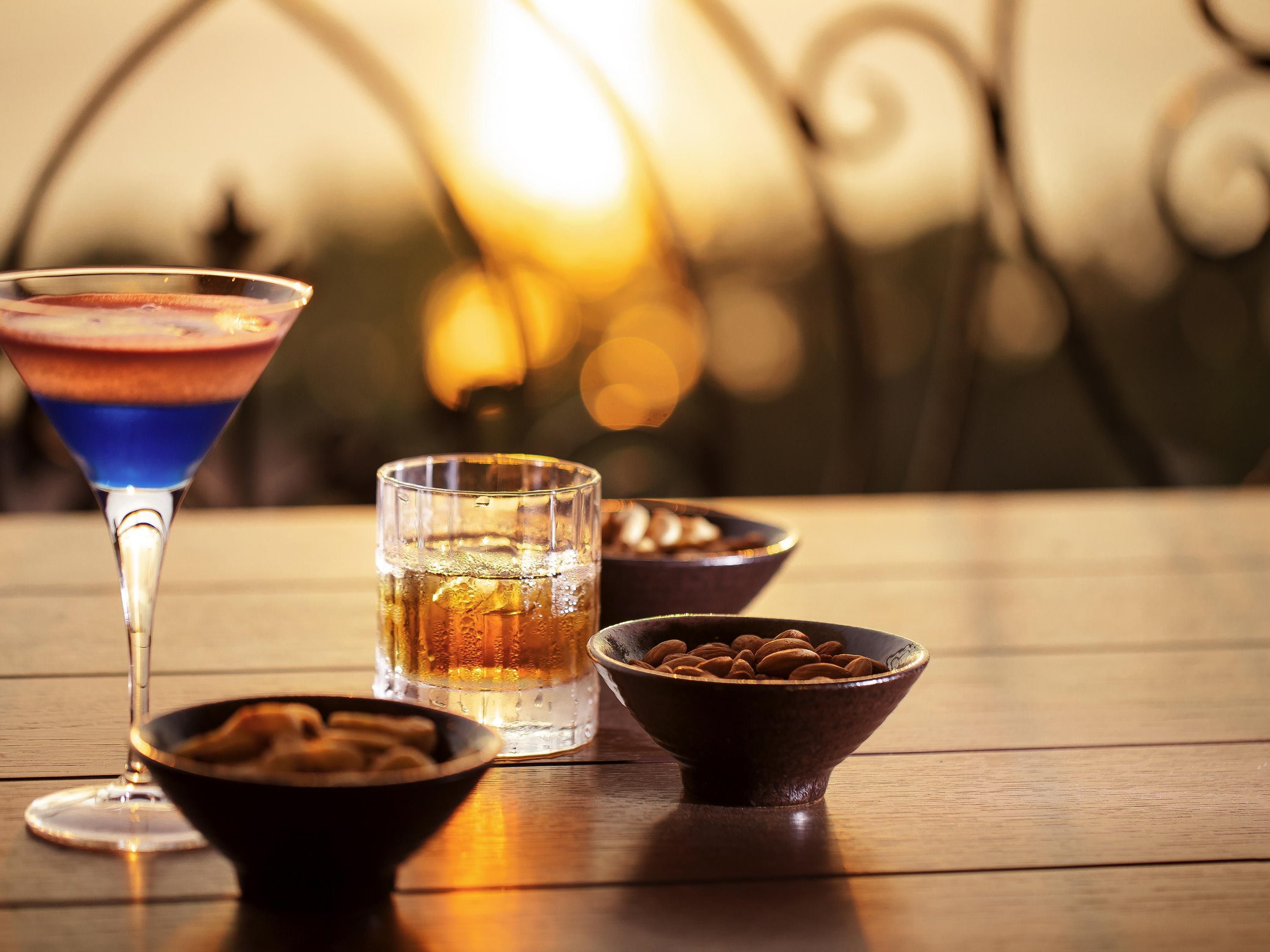 A table with a martini glass, a glass of water, and bowls of almonds.
