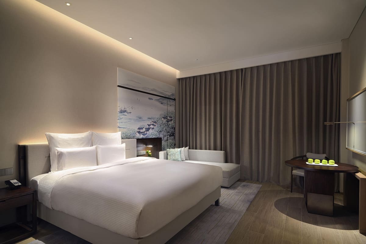 A modern hotel room with a large bed, bedside tables, a desk, and a chair.