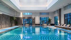 Une piscine intérieure avec un sol carrelé, des espaces de détente et de grandes fenêtres.