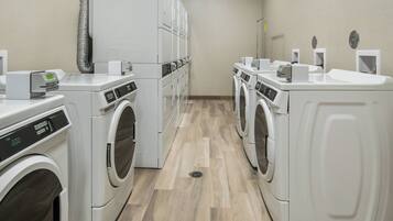 A laundry facility with multiple washing machines and dryers, a vent system, and a control panel.