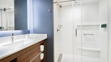 A modern bathroom with a large mirror, two sinks, a shower enclosure, and wooden cabinetry.