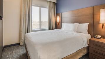 A hotel room with a large bed, a bedside table with a lamp, and a window with curtains.