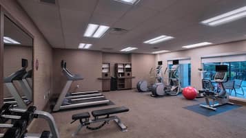 Un gimnasio con cintas de correr, elípticas, una banca y una pelota de ejercicios roja.