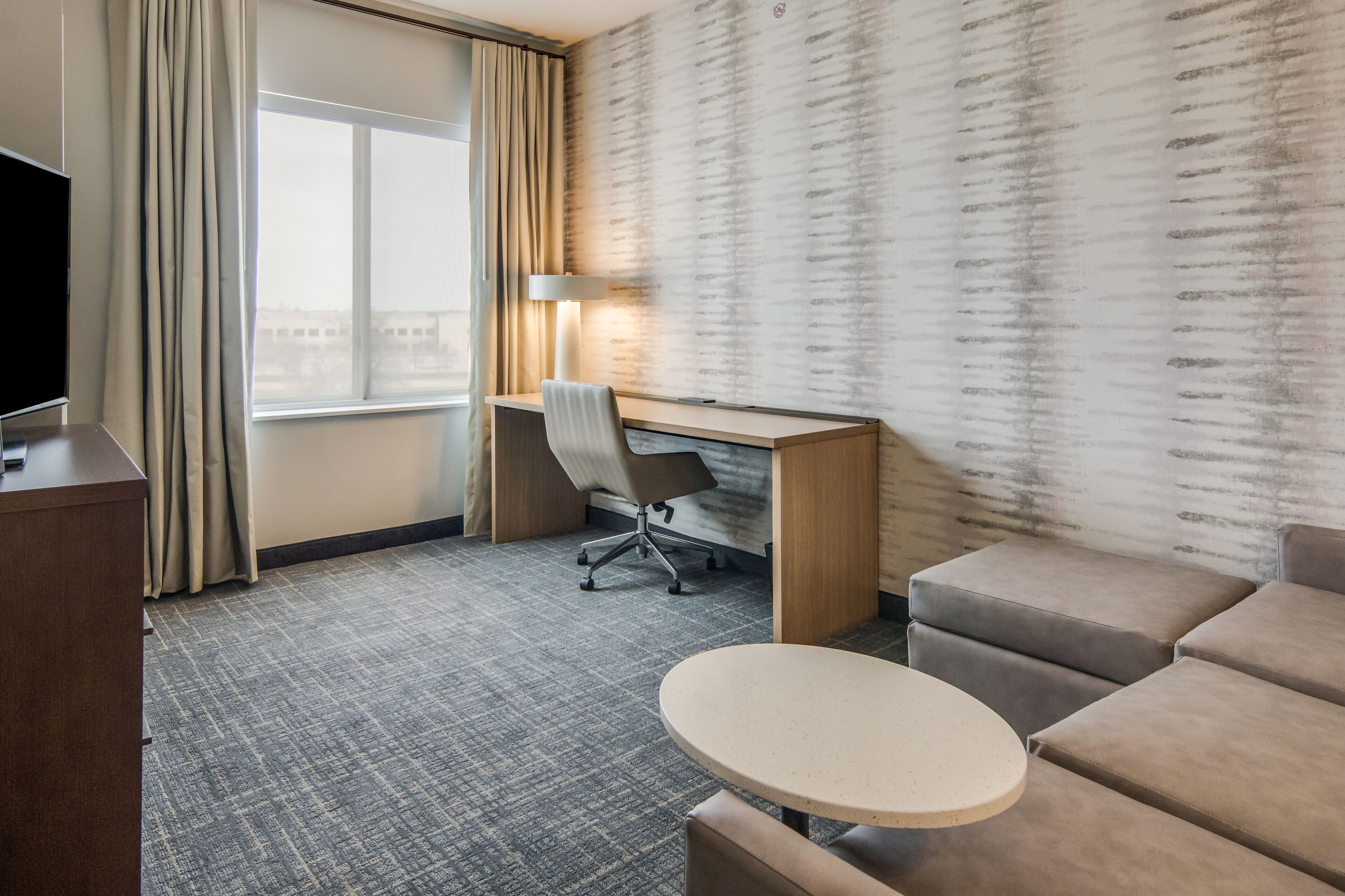 A hotel room with a desk, chair, sofa, and a small table.