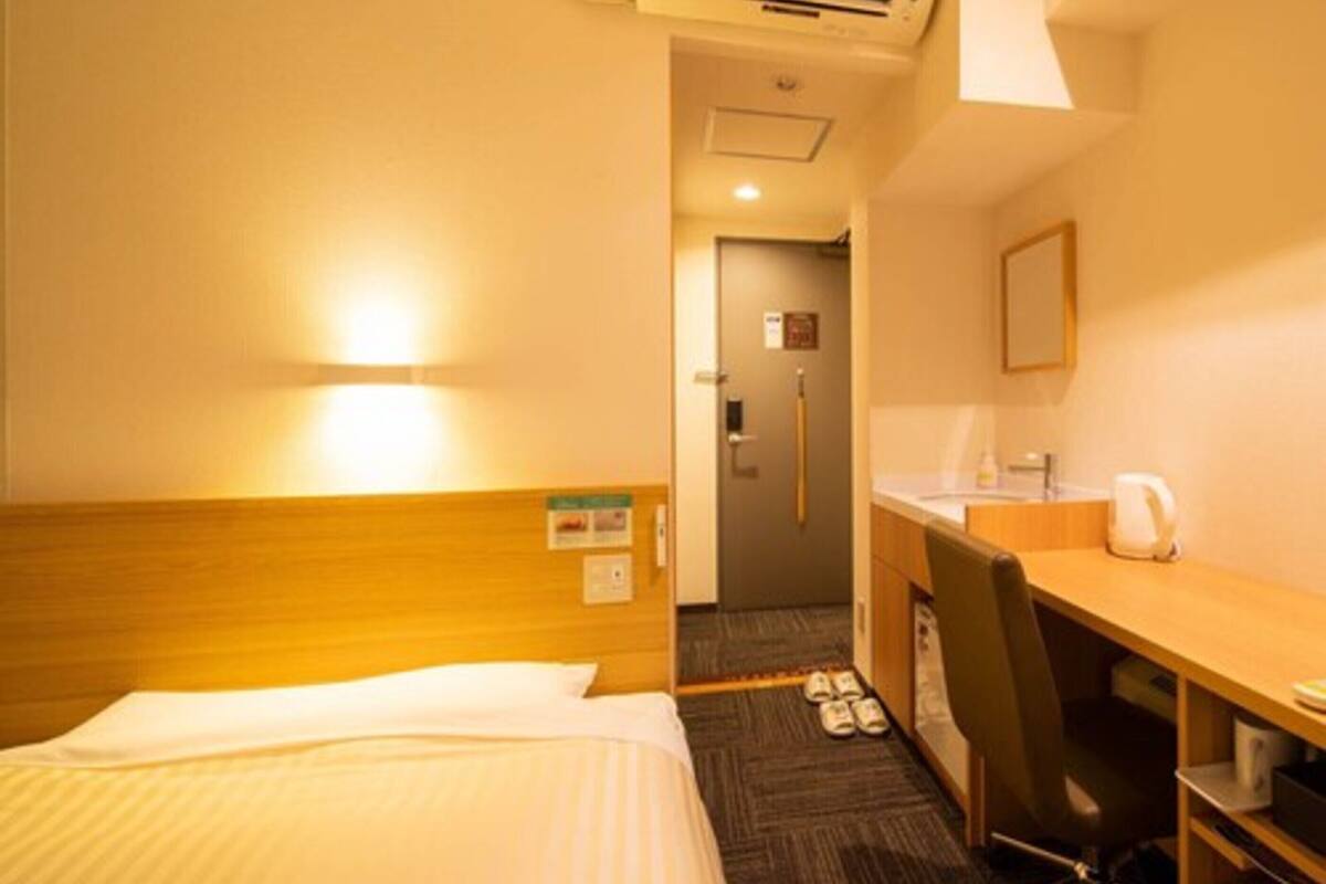 Quarto de hotel com cama, escrivaninha, cadeira, ar condicionado e pequena cozinha.