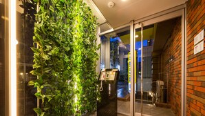 Ein Hotel Eingangsbereich mit vertikalem Grünstreifen, einer Rezeption und einer Glastür zum Innenbereich.