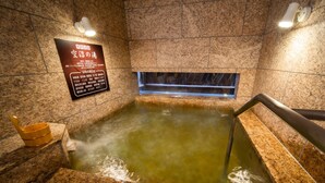 Ein Thermalbad mit Holzeimern, einem Schild mit japanischen Schriftzeichen und einem kleinen Fenster über dem Wasser.