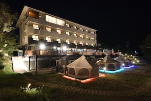A multi-story hotel with illuminated balconies and a series of tents in the foreground. - Granp Glamping Resort (Shima)