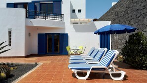 Een modern gebouw met een terras, ligbedden en een blauwe parasol.