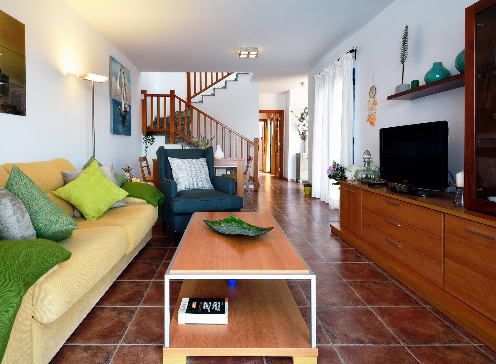 A modern living room with a sofa, armchair, coffee table, TV, and wooden staircase.