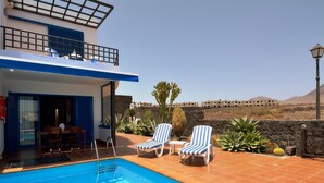 Un espace piscine comprenant deux chaises longues, une table et un escalier menant à un bâtiment doté d’un balcon.