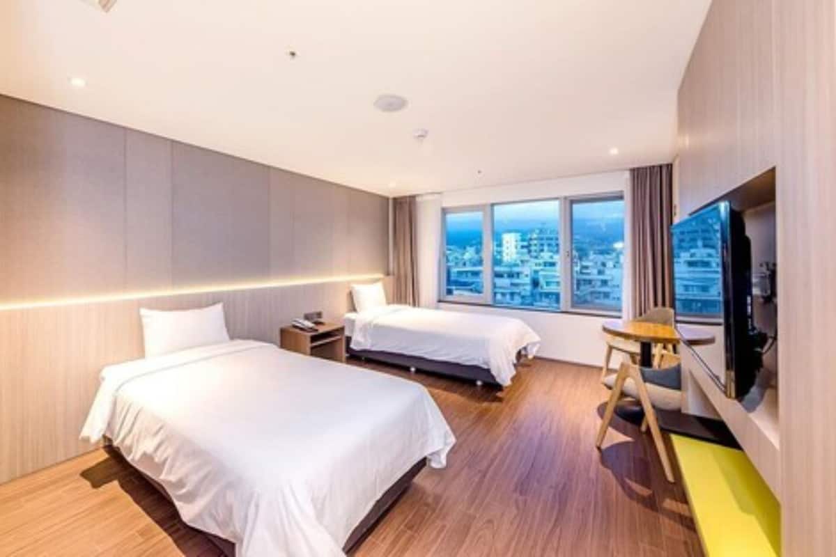 A hotel room with two beds, a TV, and a city view.
