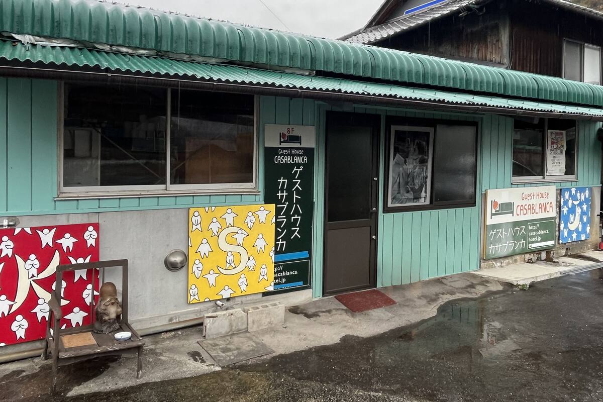 A guest house with a green exterior, a signboard with Japanese text, and a red and yellow poster on the wall.