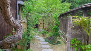 Ein traditioneller japanischer Garten mit einem Holzweg, einem Bambuszaun und einem Gebäude mit einem Reetdach.