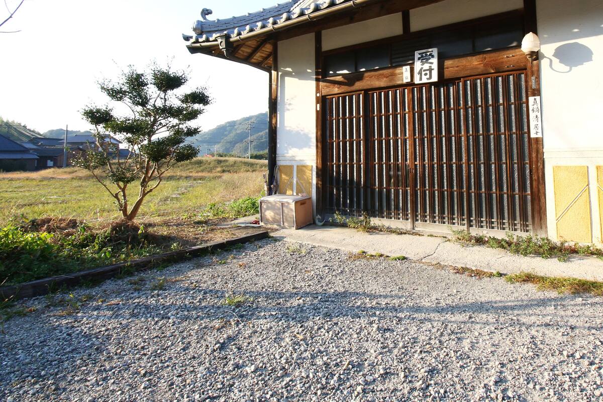 A traditional building with a wooden gate, a small tree, and a gravel path leading to the entrance.