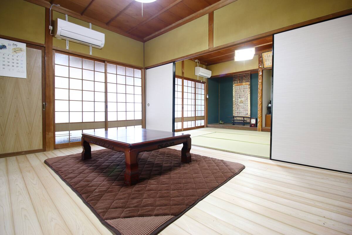 A traditional Japanese room with tatami flooring, a low wooden table, sliding doors, and a view of a tatami mat room.