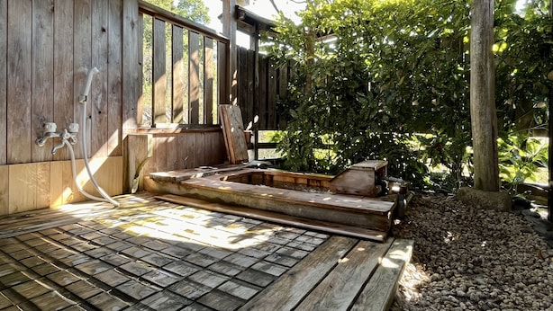 Eine Holzterrasse mit Whirlpool und einer Holzbank, umgeben von viel Grün.