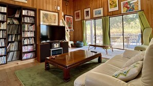 Ein Zimmer mit Holzwänden, einem Bücherregal, einem Fernseher, einem Sofa und einer Essecke mit Tisch und Stühlen.