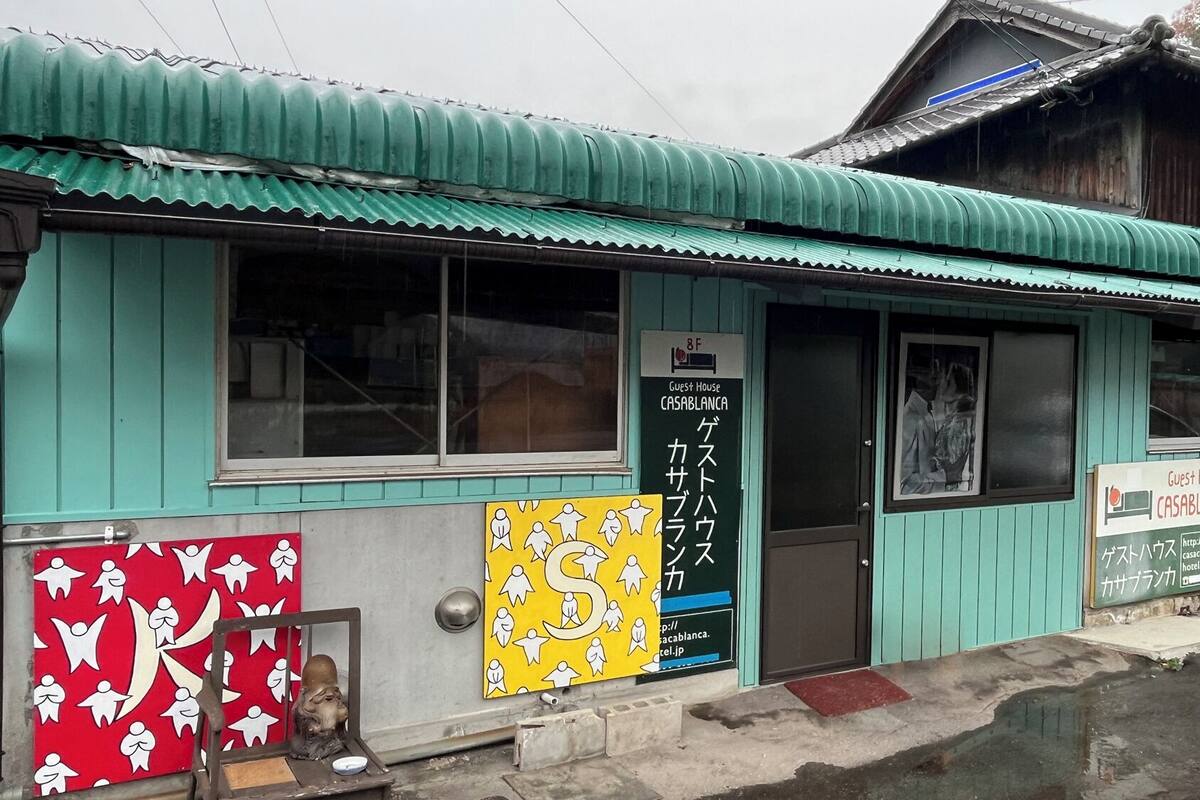 A guest house with a green exterior, a signboard with Japanese text, and a small entrance.