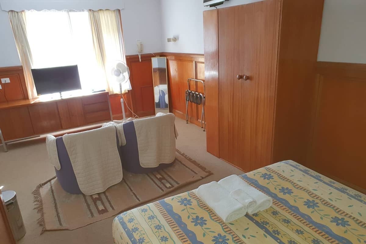 A hotel room with a bed, a desk, a chair, a mirror, and a wardrobe.